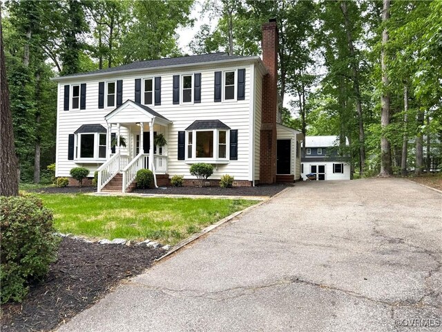 colonial home featuring a chimney and asphalt driveway