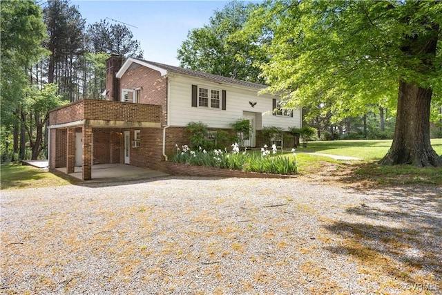 bi-level home with brick siding, driveway, a chimney, and a carport