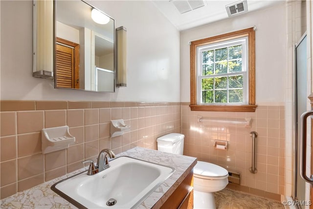 bathroom featuring tile walls, toilet, visible vents, and a stall shower