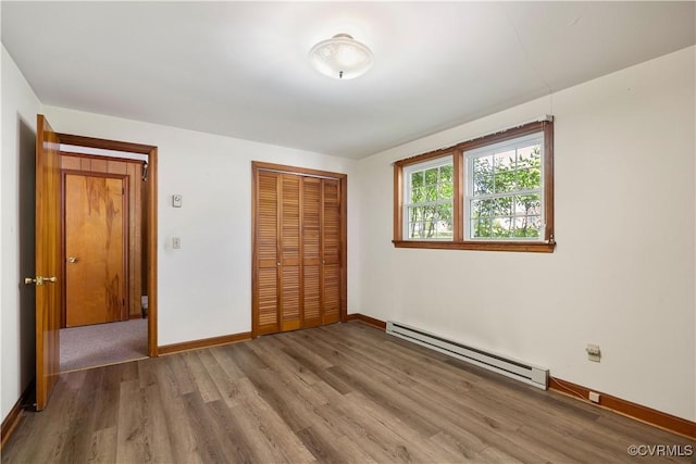 unfurnished bedroom featuring baseboards, baseboard heating, a closet, and wood finished floors