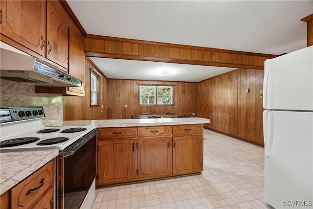 kitchen featuring wood walls, light countertops, a peninsula, under cabinet range hood, and white appliances
