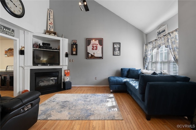 living area featuring a glass covered fireplace, high vaulted ceiling, and wood-type flooring