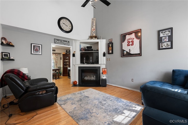 living area featuring wood finished floors, a ceiling fan, a fireplace with flush hearth, and a high ceiling