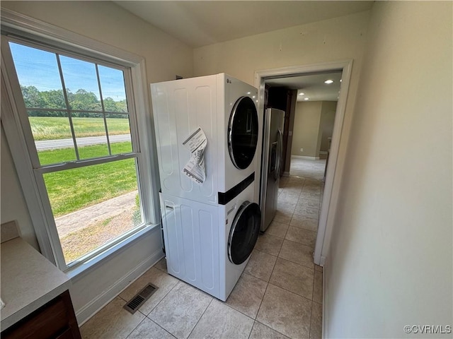 clothes washing area with visible vents, stacked washer and dryer, baseboards, and light tile patterned floors