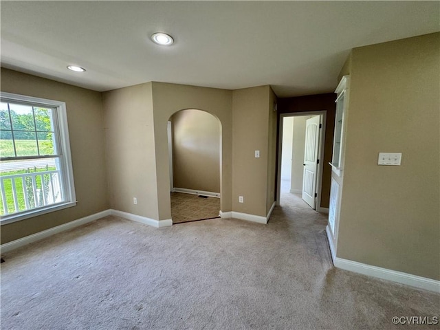 spare room with arched walkways, baseboards, light carpet, and recessed lighting