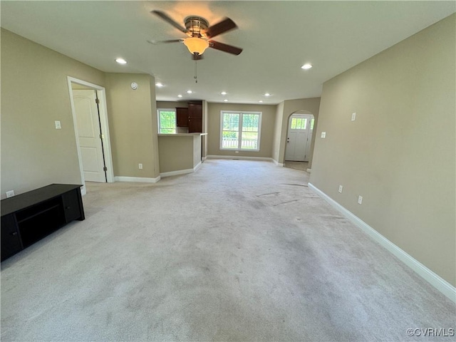 unfurnished living room with ceiling fan, light carpet, arched walkways, recessed lighting, and baseboards
