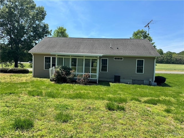 rear view of house featuring central air condition unit, a lawn, a sunroom, and roof with shingles