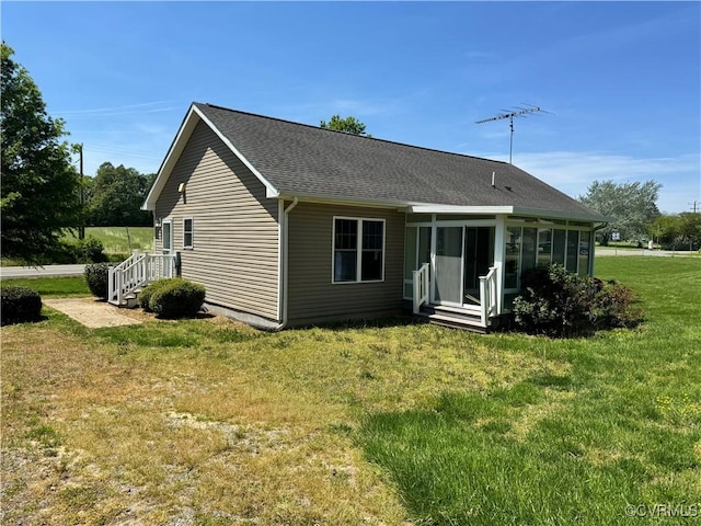 rear view of property with a sunroom, roof with shingles, and a yard