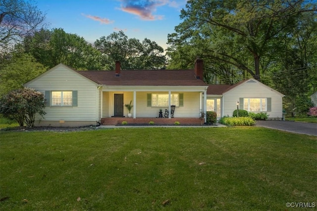 ranch-style home with covered porch, a lawn, and a chimney