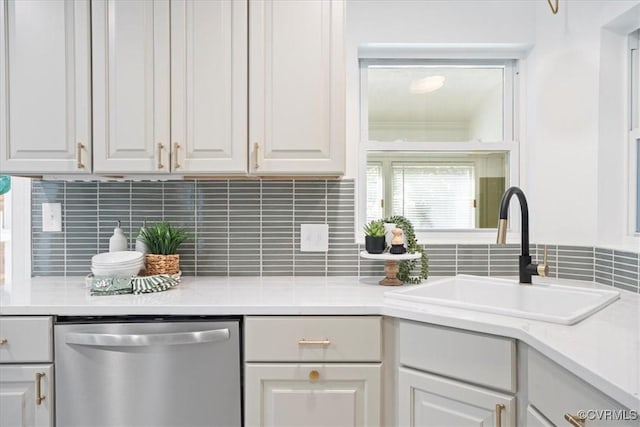 kitchen featuring tasteful backsplash, stainless steel dishwasher, a sink, light countertops, and white cabinets