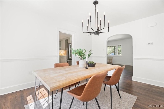 dining room featuring arched walkways, baseboards, a notable chandelier, and dark wood finished floors