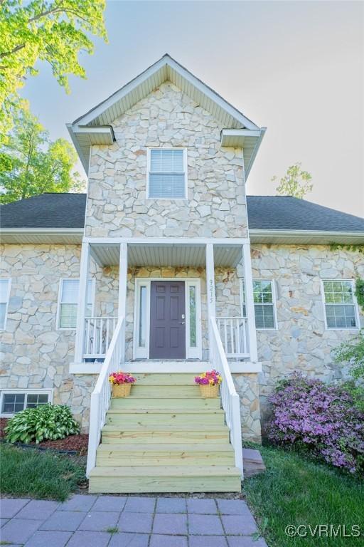 traditional-style home with covered porch, roof with shingles, and stone siding