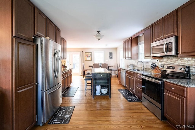 kitchen with a breakfast bar area, light wood-type flooring, dark stone counters, a sink, and appliances with stainless steel finishes