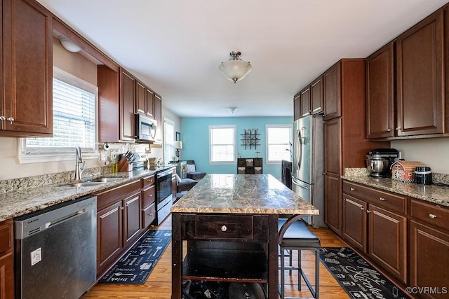 kitchen with a kitchen island, light wood-type flooring, light stone counters, a sink, and stainless steel appliances