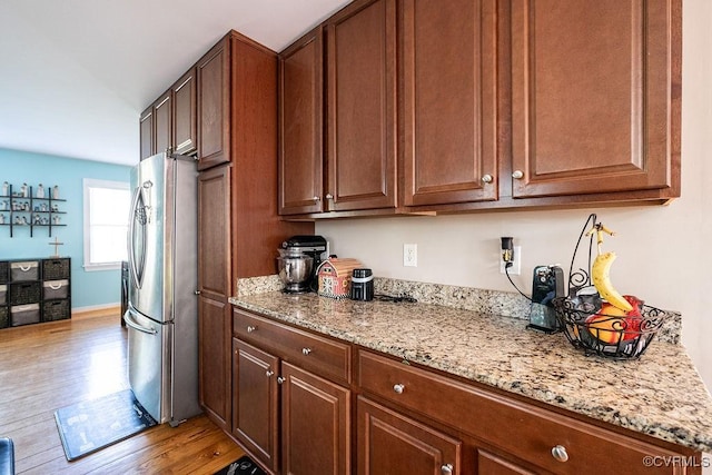 kitchen featuring baseboards, freestanding refrigerator, light wood-style flooring, and light stone countertops