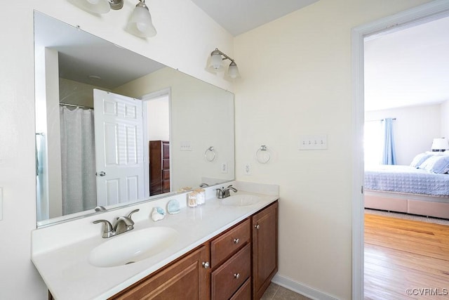 ensuite bathroom featuring a sink, baseboards, double vanity, and connected bathroom