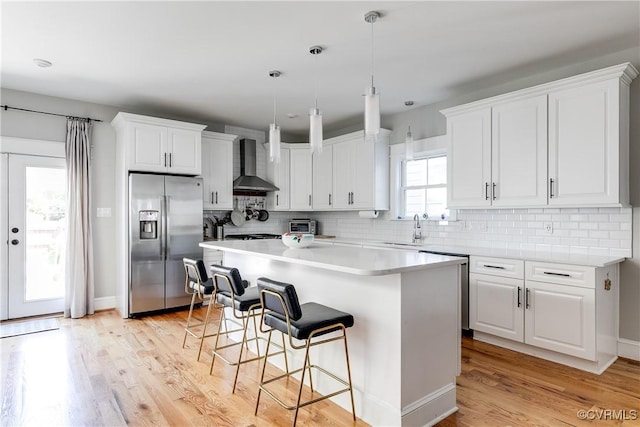 1207 N 21st St, Richmond, VA 23223 - kitchen with a breakfast bar area, stainless steel fridge, wall chimney exhaust hood, white cabinetry, and a sink