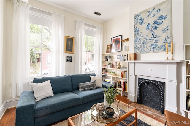living area featuring baseboards, a fireplace with raised hearth, and wood finished floors