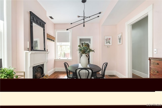 dining area featuring an inviting chandelier, a fireplace, baseboards, wood finished floors, and visible vents