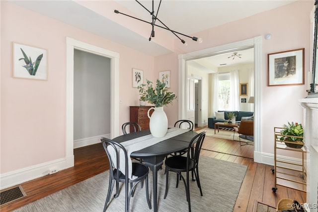 dining space featuring baseboards, hardwood / wood-style flooring, a chandelier, and visible vents
