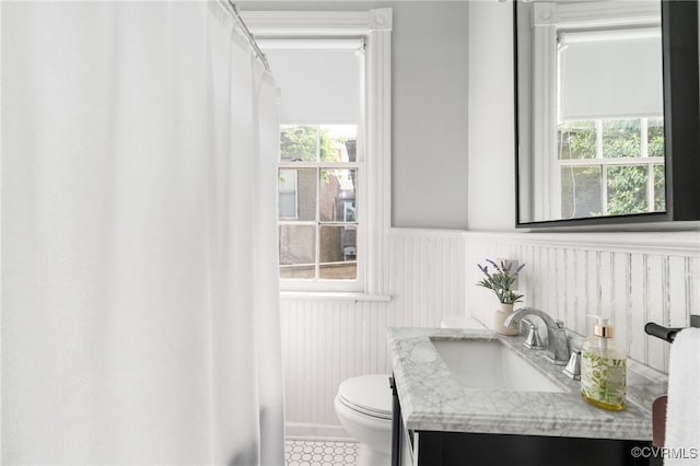full bath featuring vanity, plenty of natural light, wainscoting, and toilet