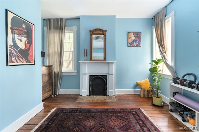 sitting room with a fireplace with flush hearth, baseboards, wood-type flooring, and visible vents