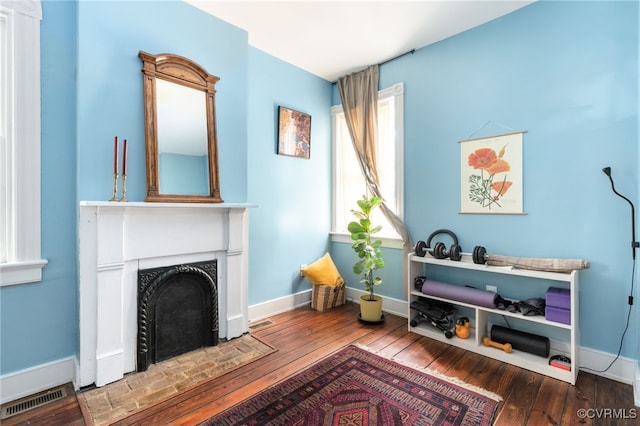 sitting room featuring wood-type flooring, baseboards, visible vents, and a fireplace with flush hearth
