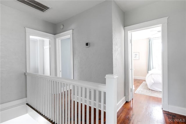 hall featuring visible vents, wood finished floors, and an upstairs landing