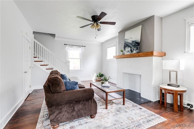 living area with ceiling fan, a brick fireplace, stairs, and wood finished floors
