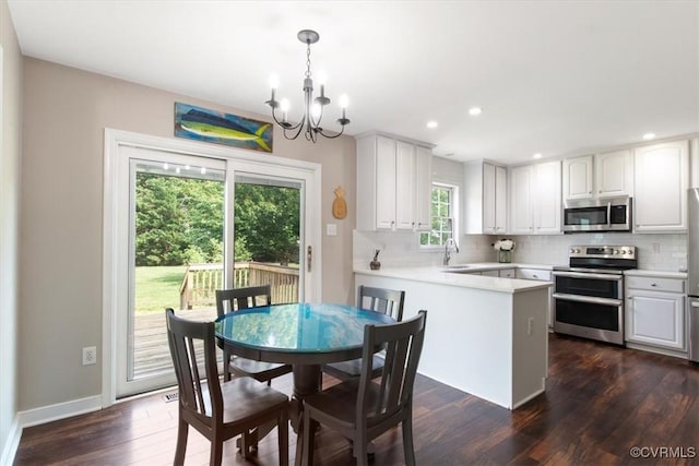 kitchen featuring a notable chandelier, dark wood finished floors, a peninsula, tasteful backsplash, and appliances with stainless steel finishes