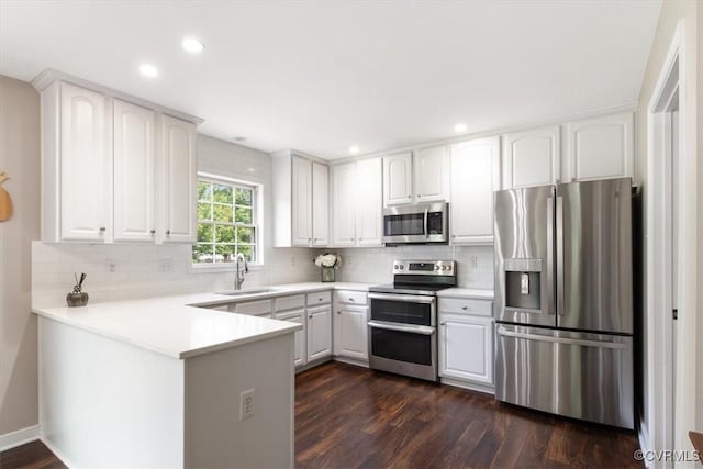 kitchen featuring a sink, a peninsula, dark wood-type flooring, stainless steel appliances, and tasteful backsplash