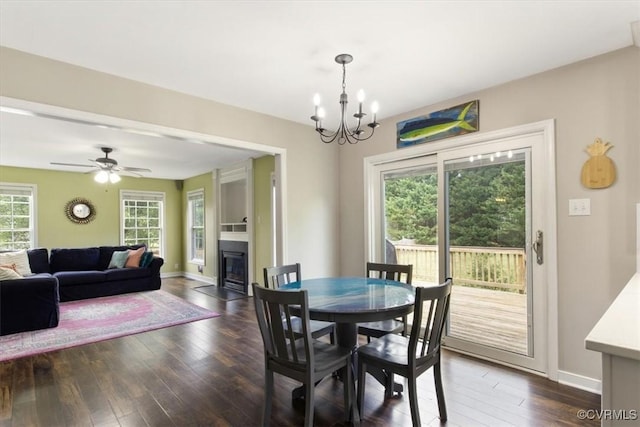 dining room with baseboards, dark wood-style flooring, a glass covered fireplace, and ceiling fan with notable chandelier