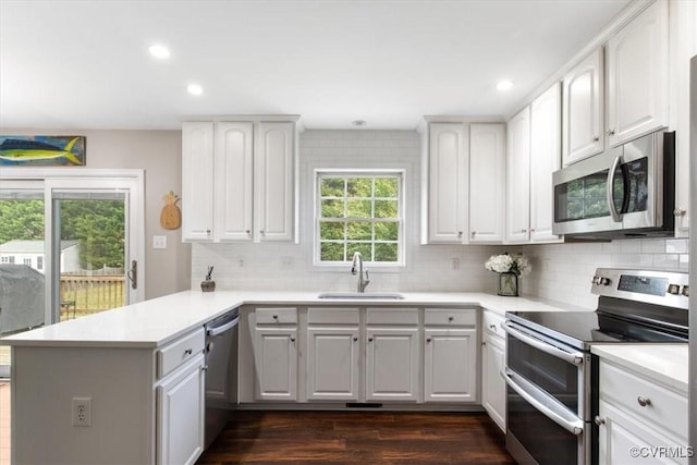 kitchen featuring a sink, a peninsula, backsplash, white cabinets, and appliances with stainless steel finishes