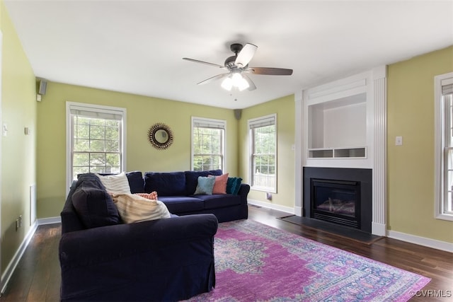 living room with a ceiling fan, a wealth of natural light, a large fireplace, and dark wood-style floors