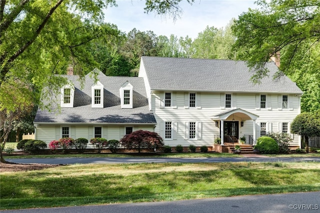 view of front of property with a shingled roof, a chimney, and a front lawn