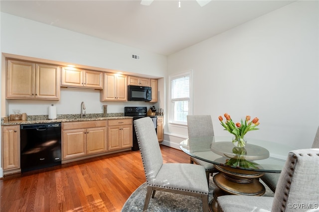 kitchen featuring light brown cabinets, light wood-style floors, light stone counters, a sink, and black appliances