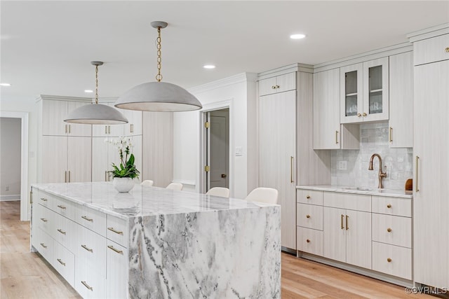 kitchen with a center island, tasteful backsplash, a sink, light wood finished floors, and ornamental molding