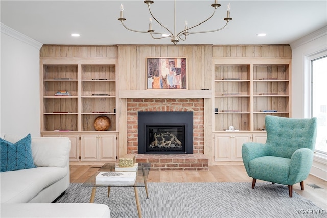 living area with an inviting chandelier, ornamental molding, a brick fireplace, and wood finished floors