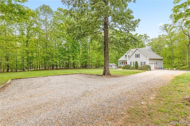 view of front of house featuring an attached garage, driveway, a front yard, and a forest view