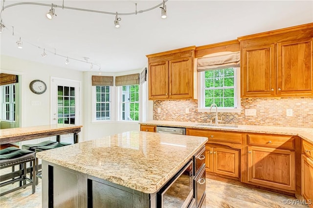 kitchen featuring decorative backsplash, brown cabinetry, built in microwave, a sink, and light stone counters
