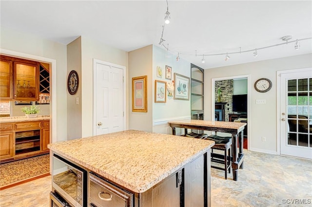 kitchen featuring a center island, track lighting, light stone counters, baseboards, and stainless steel microwave