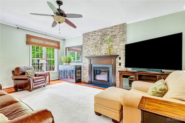 living area with crown molding, ceiling fan, a stone fireplace, and wood finished floors