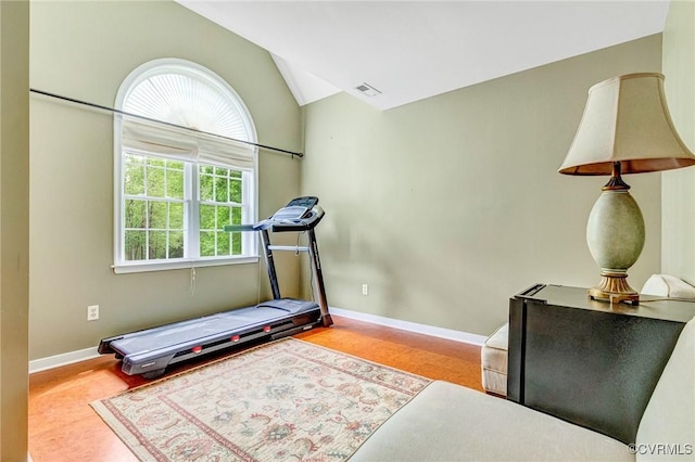exercise room featuring baseboards, vaulted ceiling, and visible vents