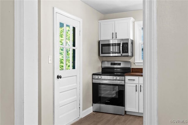 kitchen featuring wood finished floors, dark countertops, baseboards, white cabinets, and appliances with stainless steel finishes