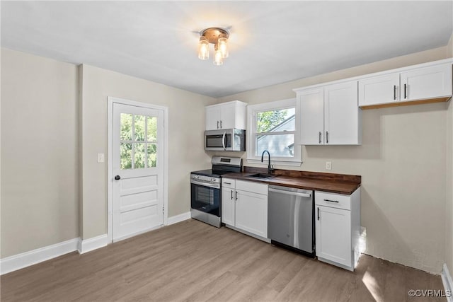 kitchen featuring a sink, wood counters, stainless steel appliances, white cabinetry, and light wood-type flooring