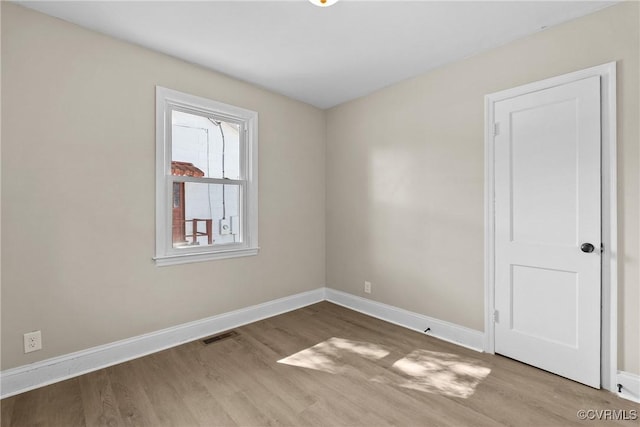 spare room featuring baseboards, visible vents, and wood finished floors