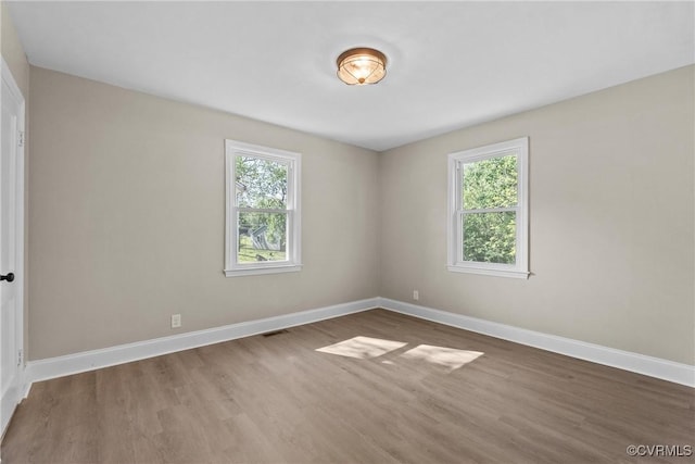 spare room with baseboards, visible vents, plenty of natural light, and wood finished floors