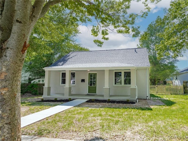 bungalow-style home with covered porch, roof with shingles, a front yard, brick siding, and fence