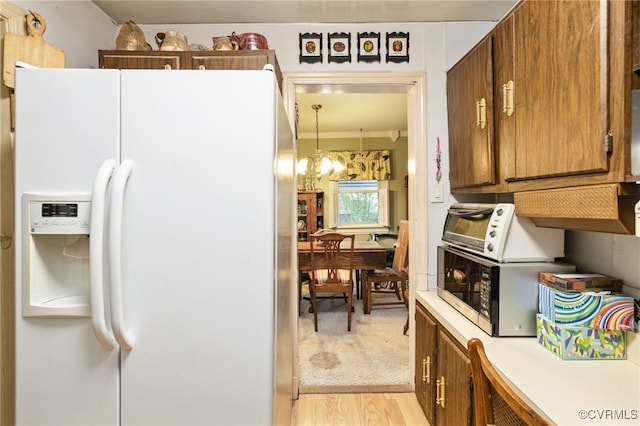 kitchen featuring an inviting chandelier, a toaster, white refrigerator with ice dispenser, light countertops, and brown cabinets
