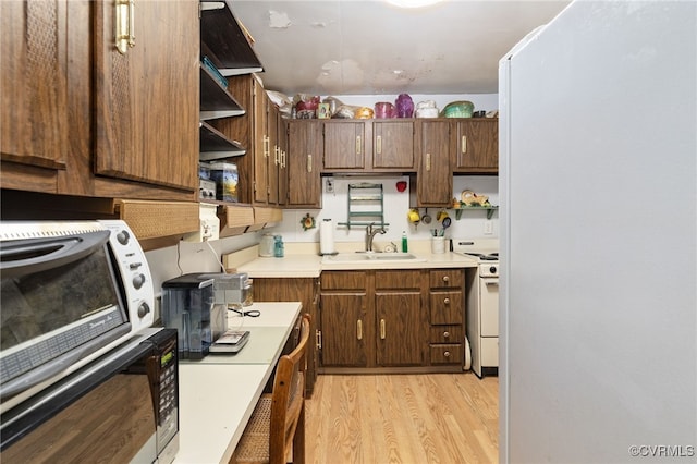 kitchen with open shelves, white gas range oven, light countertops, a sink, and light wood-style flooring
